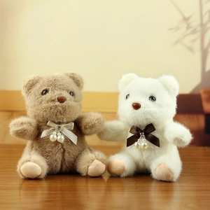 Detail view of plush bears with satin bows and pearl charms on a wooden surface