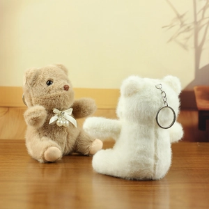 Detail of plush bear keychains in brown and white with ribbon pearls on wooden surface
