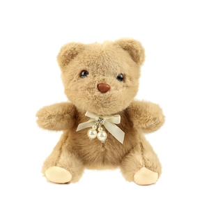 Cute light brown plush bear keychain with cream ribbon bow and pearl details on white background