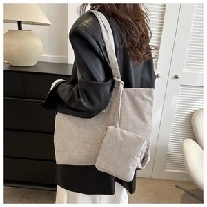 A detailed macro view of a large gray corduroy tote bag with its matching zip pouch