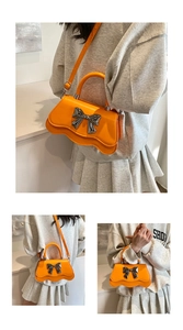 Détail du sac orange avec nœud argenté, bords ondulés et cuir synthétique lisse