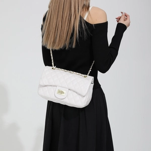 White quilted shoulder bag with gold chain strap worn by a model in a studio setting