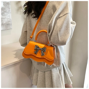 Détail d'un sac à main orange brillant avec nœud en métal argenté et bords ondulés