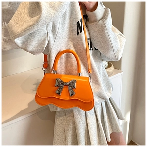 Mannequin portant un sac bandoulière orange vif avec nœud argenté et bord ondulé
