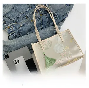 Detail of floral tote bag with pink blossoms and green tassel next to a tablet