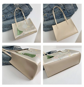 Detail view of beige Chinese style tote bag with floral patterns and green tassel pendant