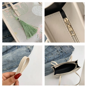 Detail view of floral tote bag showing metal zipper, tassel charm and reinforced handles