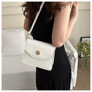 Détail du sac bandoulière blanc en cuir avec fermoir doré sur modèle en robe noire