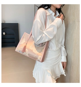 Close-up of pink silk tote bag featuring white floral embroidery and tassel detail