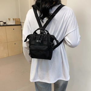 Rear view of a black mini canvas backpack with SPORT label on a female model