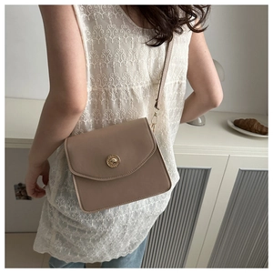 Détail d'un petit sac bandoulière beige minimaliste avec boucle dorée vintage sur un modèle
