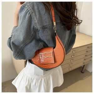Detail of orange crescent bag with crocodile texture and gold buckle on a model