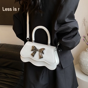 Petit sac à main blanc avec nœud argenté et bords ondulés porté sur un blazer noir