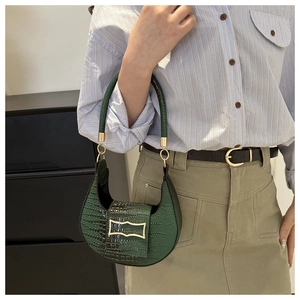Detail of dark green crocodile pattern handbag with gold hardware and top handle