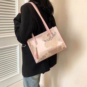 Pink satin tote bag with exquisite floral embroidery and tassel detail in soft lighting