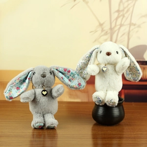 Detail of grey and white plush rabbits with floral patchwork and heart pendants on wood