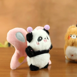 Close-up of a panda plush charm with purple antennae and pink wings on a wooden surface