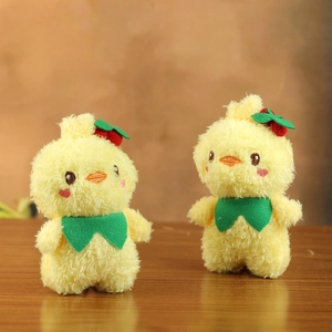 Detail of two plush yellow duckling keychains with green bows and embroidery on wood