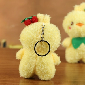 Detail of yellow plush chick keychain with metallic link and cherry decor on wood