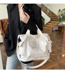 Model wearing a large off-white canvas tote bag with multiple pockets and fashion label