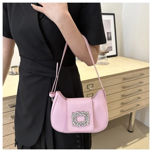 Sac à bandoulière rose en cuir avec boucle en cristal porté sur un costume noir