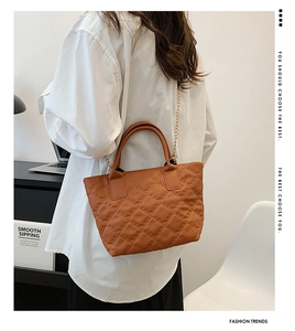 Borsa a secchiello marrone trapuntata con catena dorata mostrata su una modella in ufficio