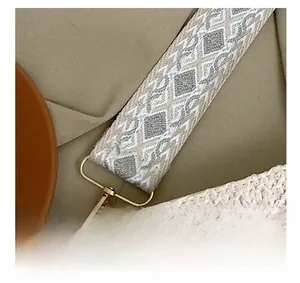 Detail of straw woven bag featuring embroidered geometric strap and gold-tone hardware