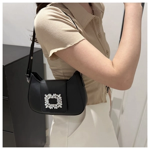 Sac baguette noir chic avec boucle en strass porté par un mannequin en intérieur