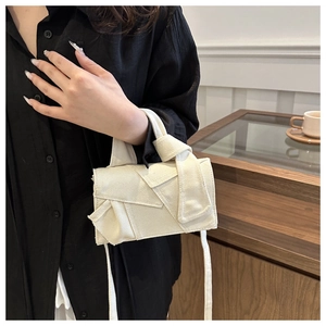 Détail d'un sac bandoulière beige en toile avec rabat à bords francs et nœud