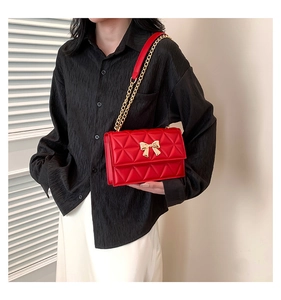 Detail of red quilted crossbody bag featuring a gold bow clasp and chain strap