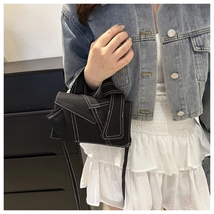 Détail du sac bandoulière en toile noire avec coutures contrastées et design déconstruit