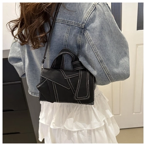 Détail du sac à bandoulière en toile noire avec surpiqûres blanches et design déconstruit