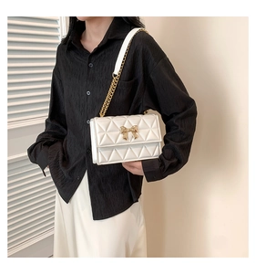 Close-up of white quilted crossbody bag with a golden bow buckle and chain strap