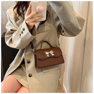 Dettaglio di borsa marrone con fibbia a fiocco argento indossata con un blazer beige