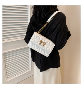 Detail of white quilted crossbody bag featuring a gold bow clasp and chain strap