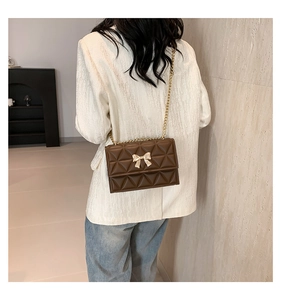 Detail of a brown quilted crossbody bag featuring a golden bow buckle and chain strap