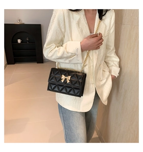 Detailed view of black quilted chain bag featuring a gold bow-knot metal clasp detail