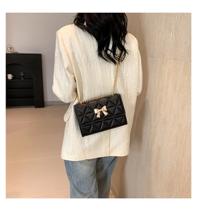 Detail of black quilted crossbody bag with gold bow clasp and elegant chain strap on model