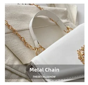 Détail du sac en cuir blanc avec décor de fleur dorée, perles et bandoulière chaîne