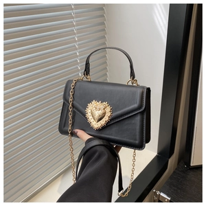Détail d'un sac enveloppe noir avec fermoir coeur doré et bandoulière en chaîne