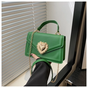Détail du sac bandoulière vert montrant la boucle cœur vintage et la fine chaîne dorée