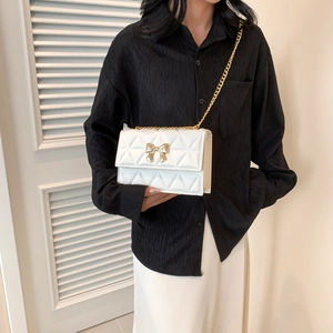 Weiße gesteppte Schultertasche mit goldener Schleife und Kette am Modell