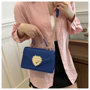 Détail d'un sac à bandoulière bleu avec fermoir coeur doré porté par un mannequin