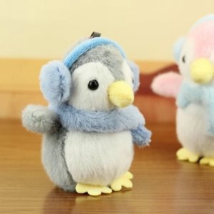 Close-up of cute penguin plush keychain featuring blue earmuffs and a cozy winter scarf