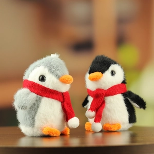 Close-up of plush penguin couple keychains with cozy red scarves on wooden surface