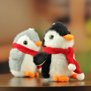 Close-up of cute grey and black plush penguin keychains with red scarves on wood