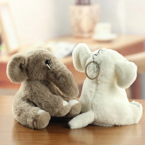 Close-up of soft plush elephant keychains in brown and white on a wooden surface