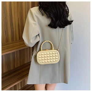 Close-up of golden waffle texture box bag with twisted metal handle and fine chain