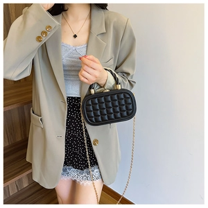 Detail of black woven texture box bag featuring a gold metal lock and elegant chain strap