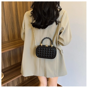 Detail of black quilted box bag with gold lock and spiral handle on a female model